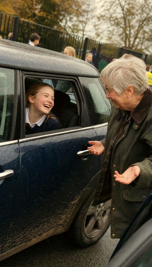 A grandmother laughing with her granddaughter at the school gates